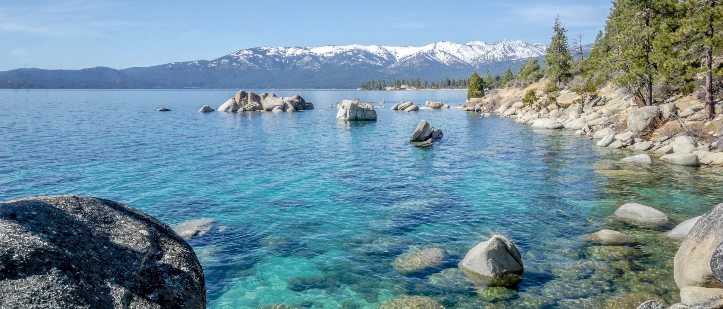A calm turquoise mountain lake with smooth rocks in the clear shallows